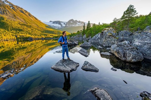 Young man standing on a rock in water, enjoying the landscape, picturesque mountain scenery in the