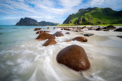 Rocks on Uttakleiv sandy beach, coast and blue sea, long exposure, rocky mountain peaks,