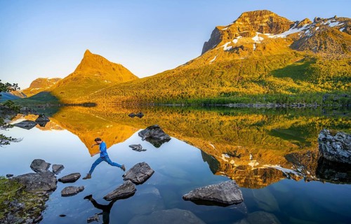 Young man jumping from stone to stone in water, picturesque mountain landscape in the Innerdalen