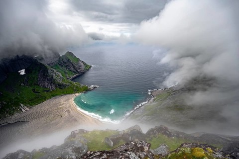 View from Helvetestinden summit, Bunesstranden sandy beach and blue sea, dramatic cloudy sky,
