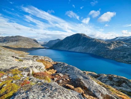 A calm lake surrounded by rocky mountains under a clear blue sky with clouds, view of Lake