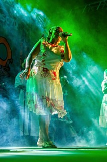 Singer wearing traditional clothes on a stage under green lights, a band playing and dancing at a