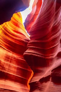 Antelope canyon's flowing sandstone walls carved by water and wind, glowing red orange as shafts of
