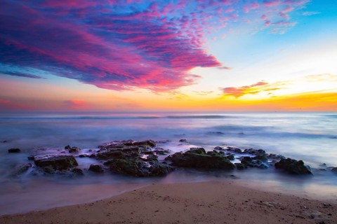 Vivid sunrise over calm coast with colorful sky and rocks in the foreground, sunset, Praia do