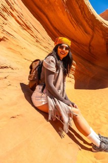 Young woman smiling while sitting on the warm sandstone of biidi the arch cave in page, arizona,