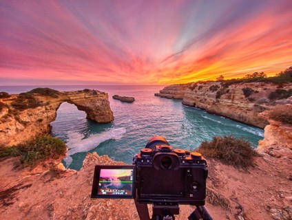 Dramatic sunset at Arco de Albandeira in Algarve, Portugal, with a camera on tripod above the