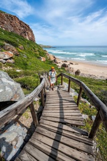 Young pretty woman wearing dress off coast and sea at Robberg Nature Reserve, Plettenberg Bay,