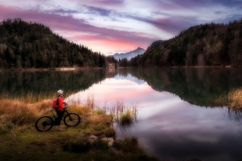 Woman with mountain bike enjoying sunrise over lake Alatsee in the eastern Allgaeu near city of
