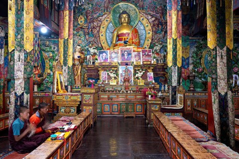 Buddhist prayer room with gilded Buddha statue, two young monks, novices recite holy mantras,