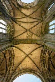 Looking up into the stone cross-rib vault of a Gothic church ruin looking at the sky through the