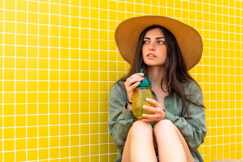 Young woman wearing a straw hat and casual shirt, relaxing outdoors with a refreshing pineapple
