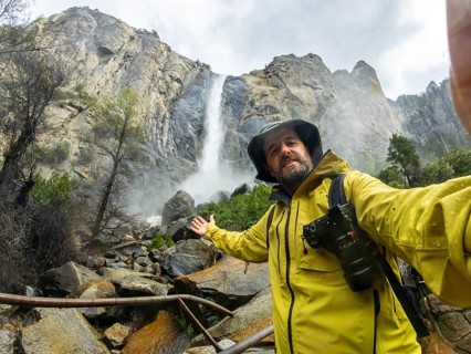 Man in a yellow raincoat and hat taking a selfie, documenting a travel adventure during a nature
