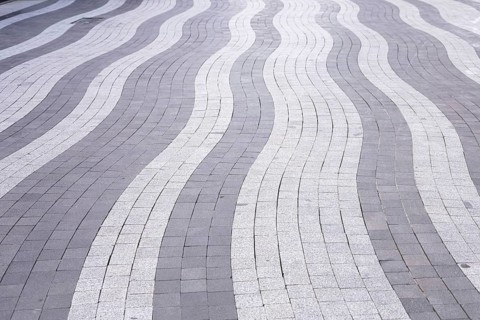 Curved lines of gray and white paving stones create an eye-catching pattern on an urban walkway.