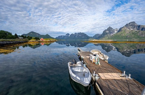 Red fishing hut on the shore and boats on a jetty, Rorbuer hut, picturesque fjord landscape at