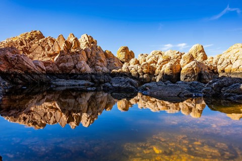 Reflection of stones in a puddle of water from the rocks on the beach at Marinedda Coast on a sunny