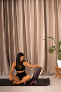 The woman interacts with a foam roller on a yoga mat, surrounded by a calm ambiance