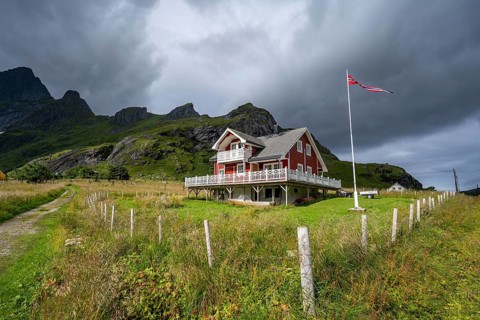 Red wooden house in green landscape, Vindstad, Reinefjord, Lofoten, Norway