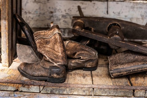 Old, worn leather boots placed on a wooden shelf. The boots are brown and show signs of age and
