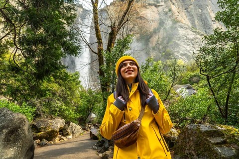Woman in a yellow raincoat and hat smiling while looking up, experiencing the refreshing mist near
