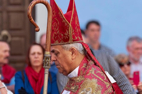 Bishop in red and gold garb during a religious procession surrounded by people, Good Friday