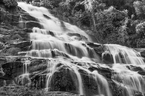 Mae Ya waterfall with cascading flowing water framed by lush tropical vegetation, black and white
