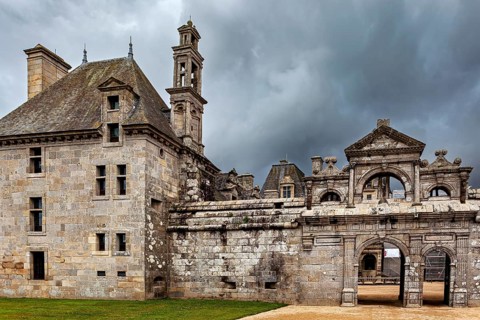 An old stone building with a gate under ominous grey clouds, The Château de Kerjean Castle in