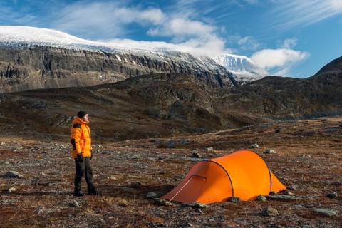 Man sitting next to tent with a view of Mount Sinnitjohkka, Kebnekaisefjäll, Norrbotten, Lapland,