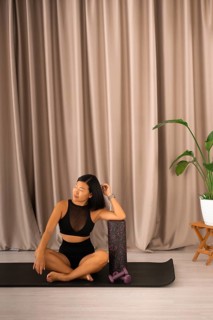 Woman meditates on a yoga mat beside a foam roller and plant, creating a serene atmosphere