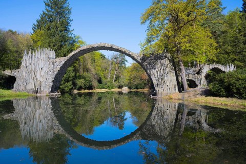 Stone bridge forms a circle with its reflection in the calm water of the forest, Rakotzbrücke,