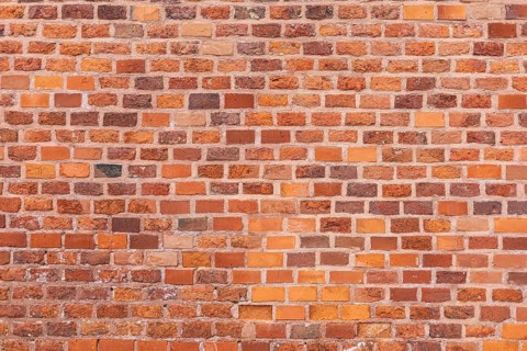 A textured wall made of red and brown bricks. The bricks vary in size and color, creating a rustic