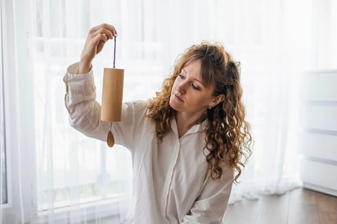 Curly-haired woman examining a wind chime in a bright, airy room
