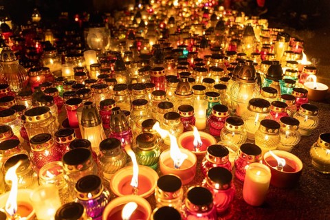 Candles glowing in colorful jars at night vigil in cemetery. A huge number of multicolored burning