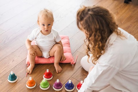 A baby and a woman engaged with colorful bells on the floor, creating a playful setting