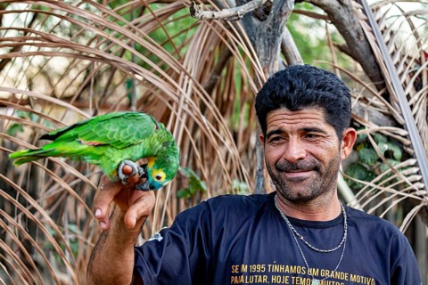 A smiling man with a parrot on his finger in a natural setting: a blue-fronted Amazon in