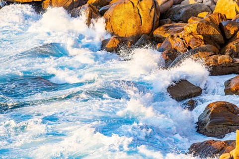Surf at the coastline, blue water flows around the stones at Costa Paradiso in eveneing light,