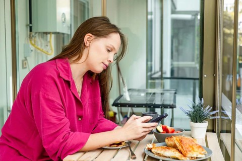 A young Caucasian woman with long brown hair sits at a table, enjoying a meal. She wears a pink