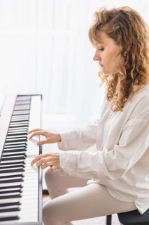 A woman intently plays the piano, bathed in soft natural light