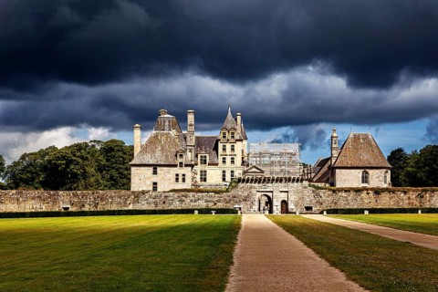 A castle in dramatic lighting with a sky surrounded by dark clouds, The Château de Kerjean Castle