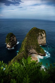 A spectacular cliff formation by the sea, with lush vegetation and calm waves, a view from above of
