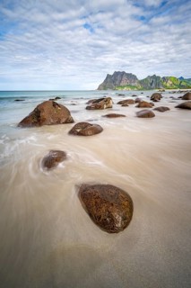 Rocks on Uttakleiv sandy beach, coast and blue sea, long exposure, rocky mountain peaks,