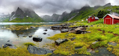 Red wooden houses on the shore in green fjord landscape with dramatic clouds, Vindstad, Reinefjord,