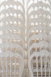 A stack of white wooden chairs arranged closely together. The chairs have intricate designs and a