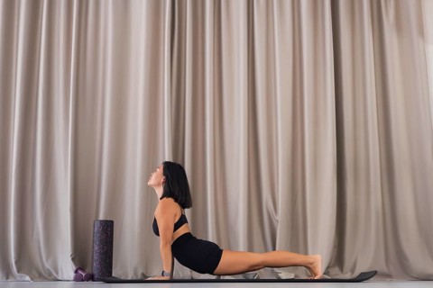 Woman practicing yoga stretching pose on a mat with neutral curtains in the background