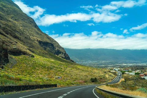 Winding asphalt road navigating along a steep green mountain slope, offering a scenic drive towards