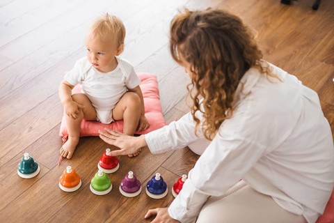 Child and mother playing with colorful xylophones on a wooden floor, engaged in an educational