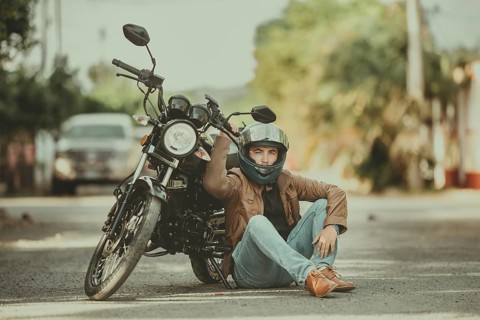 Portrait of handsome motorcyclist sitting next to his motorcycle on the road. Portrait of young