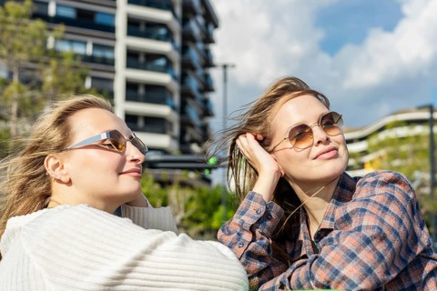 Two young women enjoying a sunny day outdoors. One has long blond hair and wears sunglasses. The