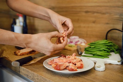 Person is removing bones from cooked salmon in kitchen. Several green beans and sliced onion are on