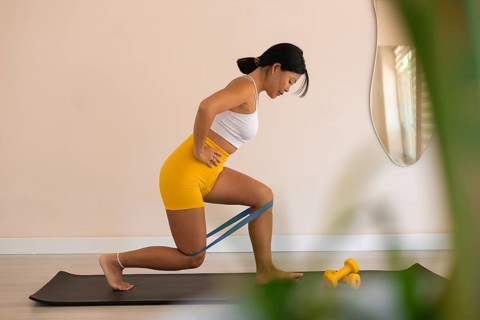Determined woman lunging with resistance band in a bright room with plants
