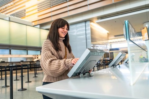 Woman smiles while using a digital self service check in kiosk at a modern airport terminal,